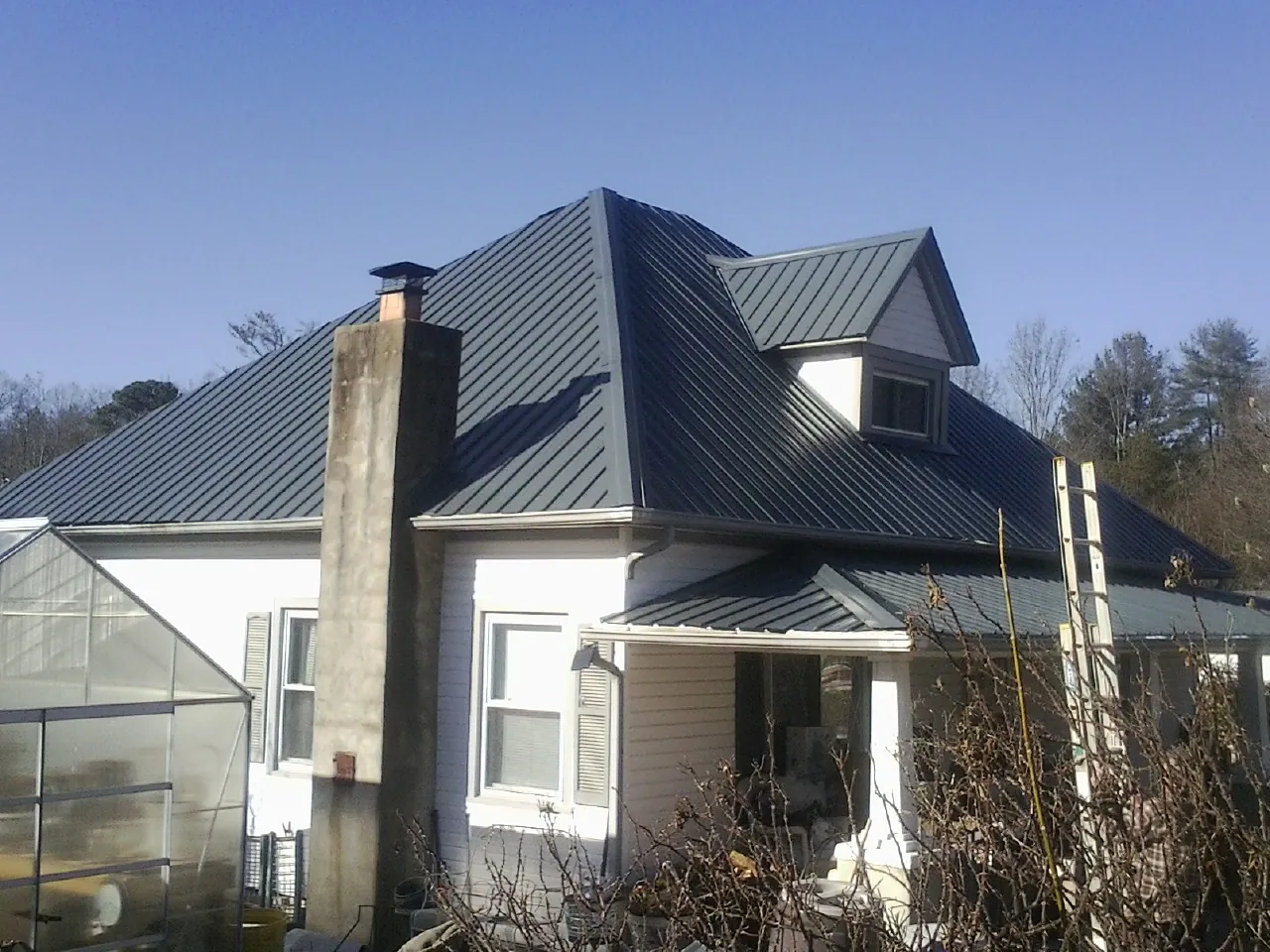 Dark blue standing seam metal roof on a white farmhouse with dormer — Slate & Tile Roof Repair by Roofing Brothers in North Franklin
