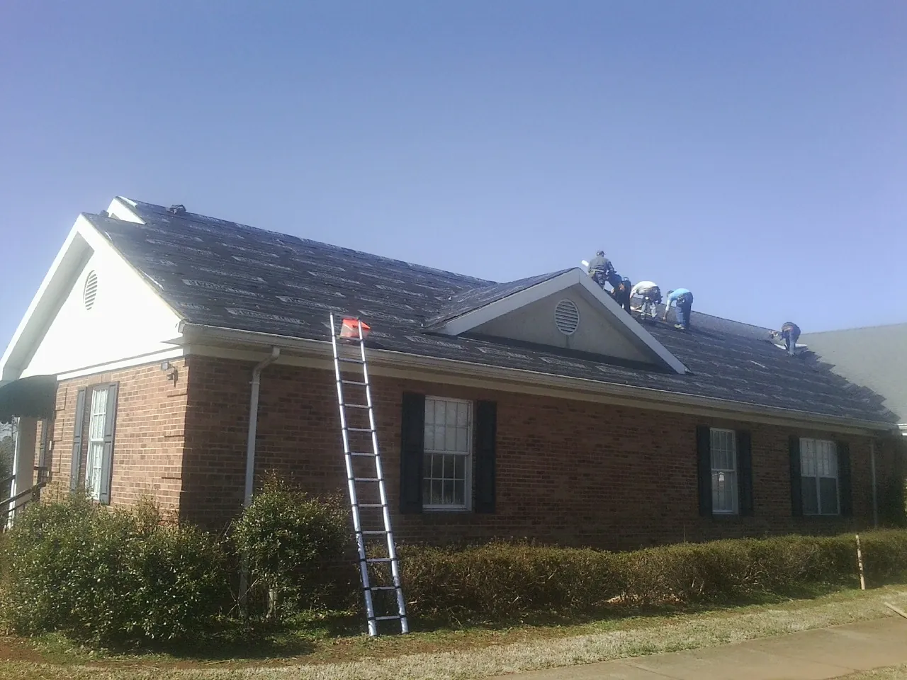 Crew tearing shingles off a brick ranch roof with a ladder set — Emergency Roof Repair work by our crew in North Franklin