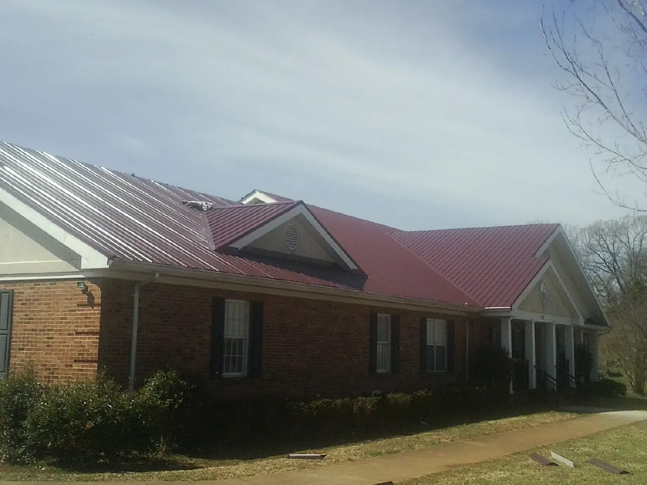 Red metal roof with gabled entries on a long brick building, from a Hail Damage Roof Repair job in North Franklin