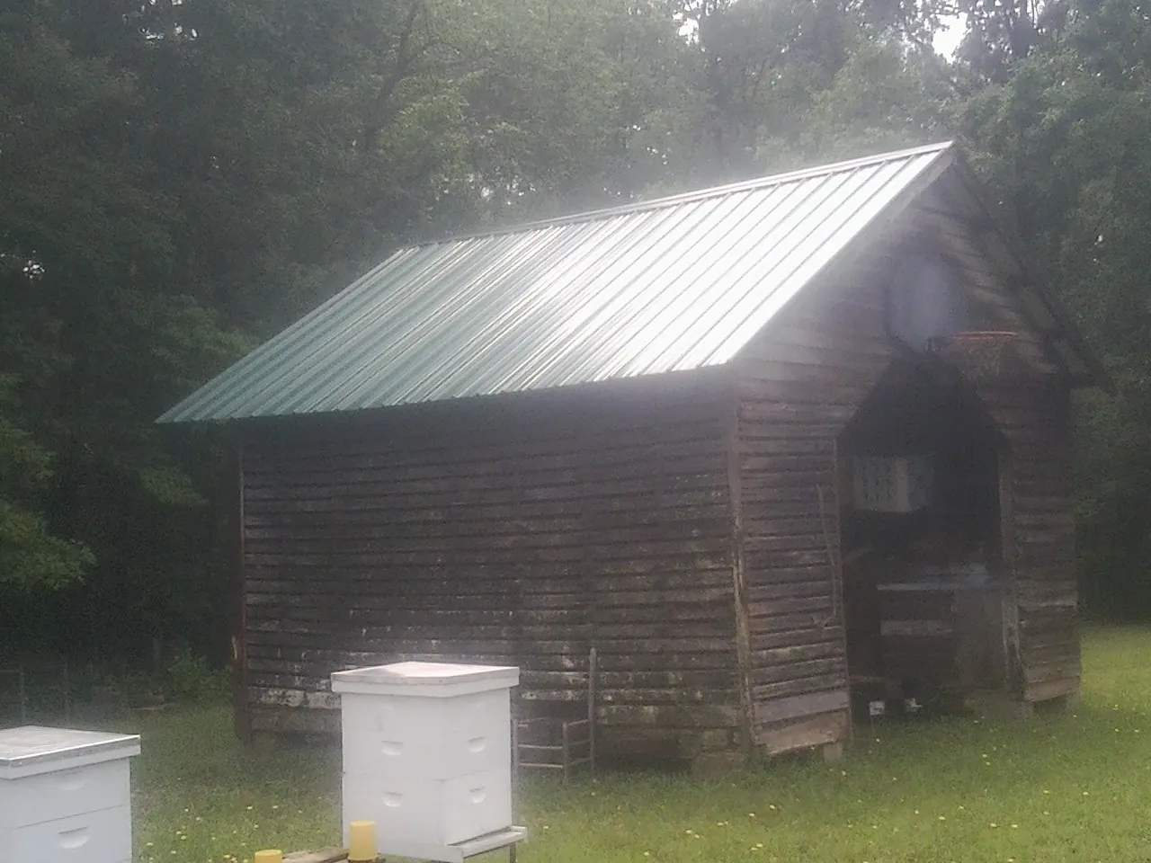 Green metal roof on a weathered barn beside stacked beehives in North Franklin