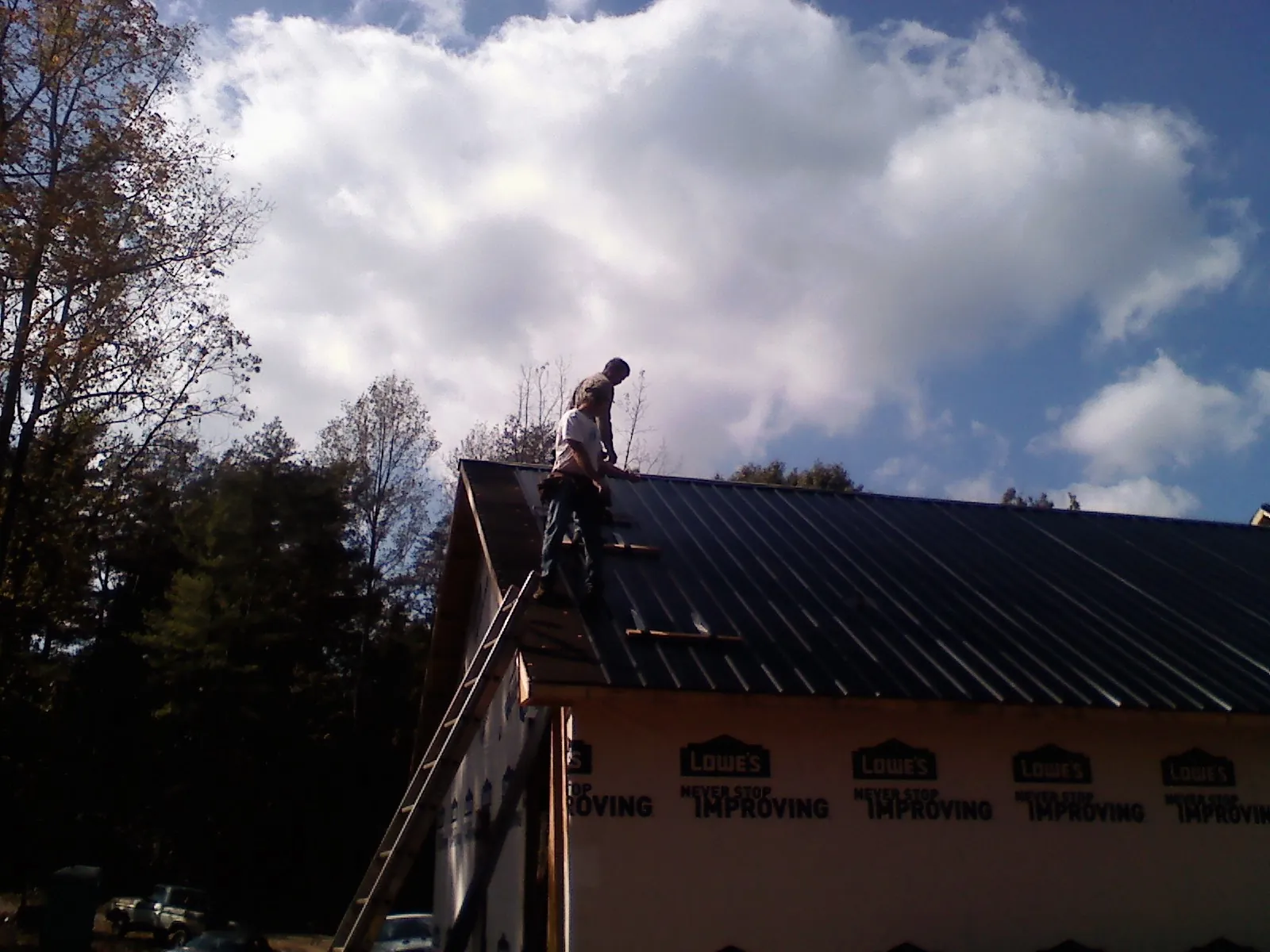 Roofer fastening dark metal panels high against a cloudy sky, from a Roof Inspection job in North Franklin