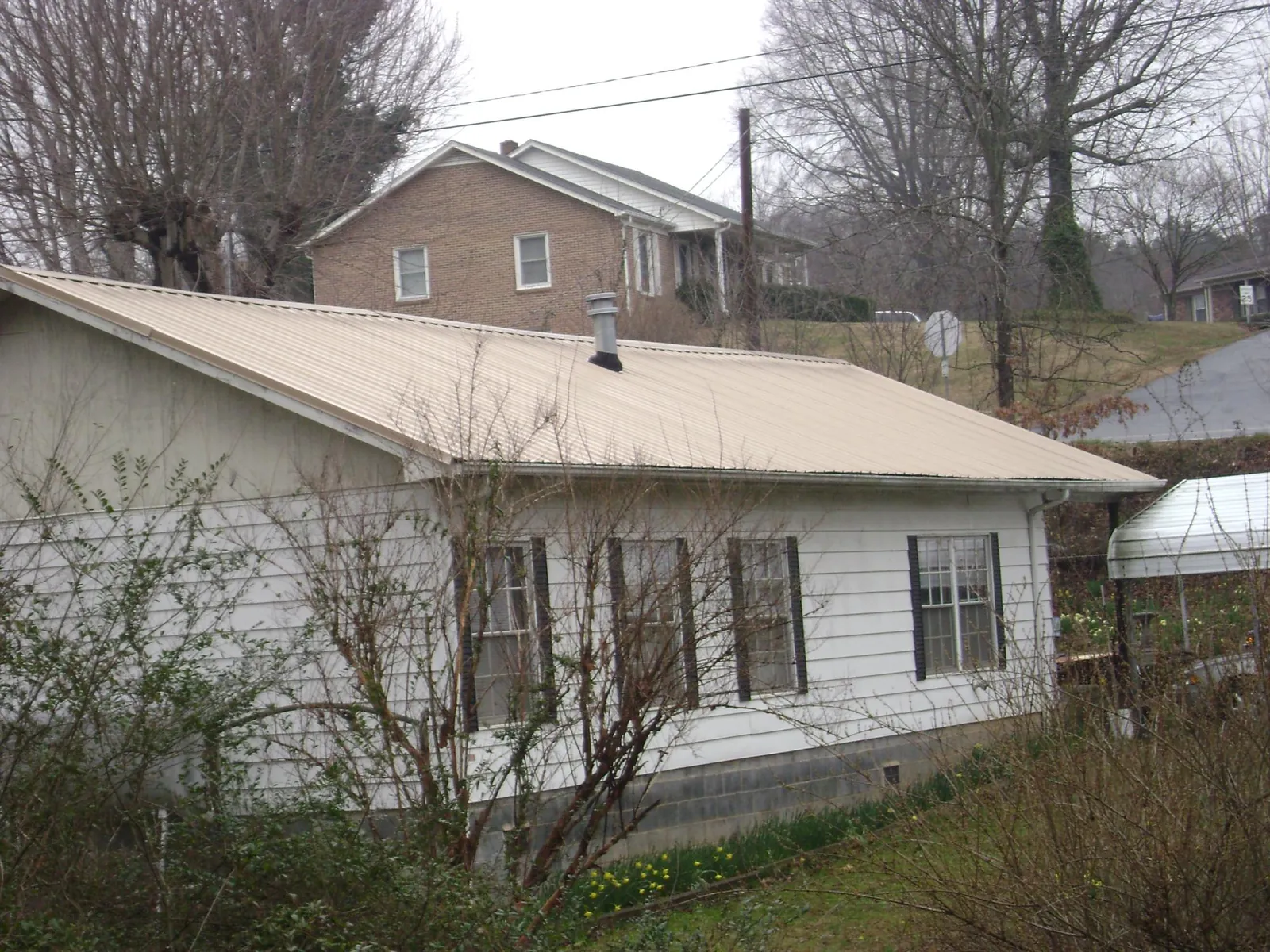 Tan metal roof on a white sided house set into a hillside — Commercial Roofing by Roofing Brothers in North Franklin