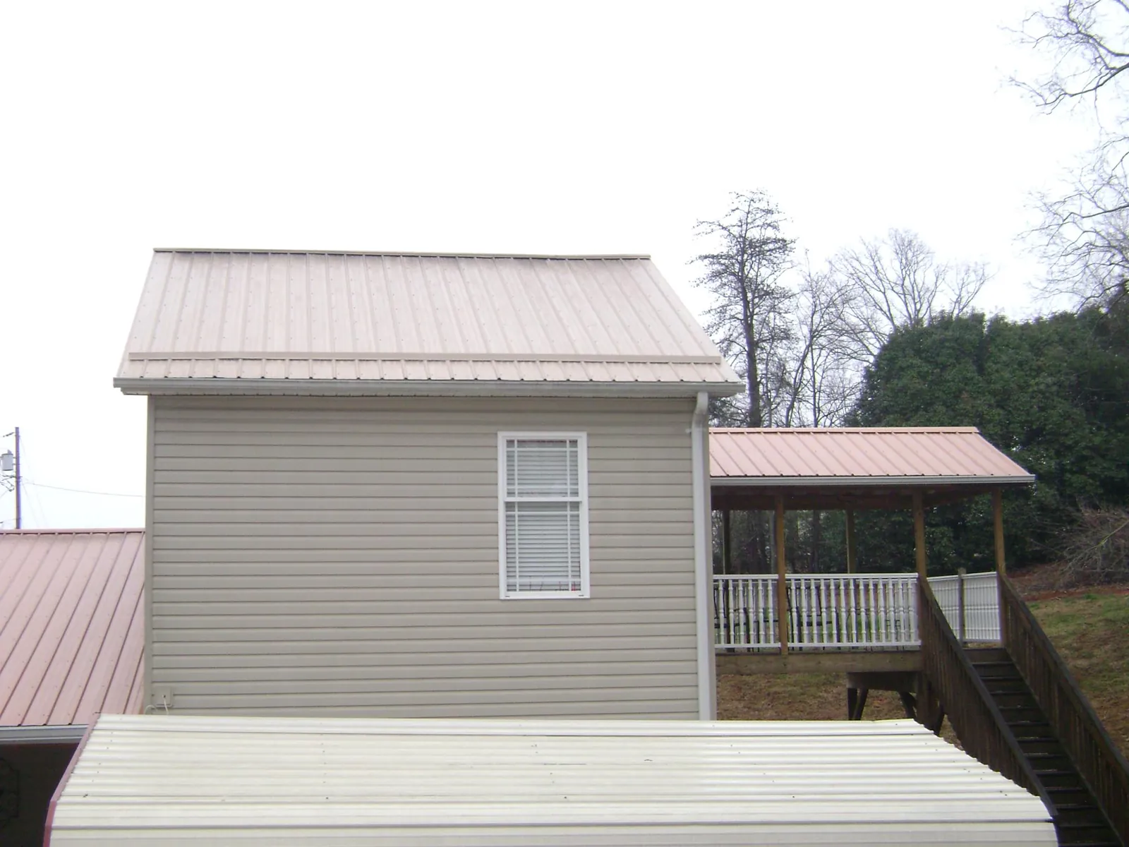 Tan metal roofs on a two story addition and attached porch, from a Roof Replacement job in North Franklin